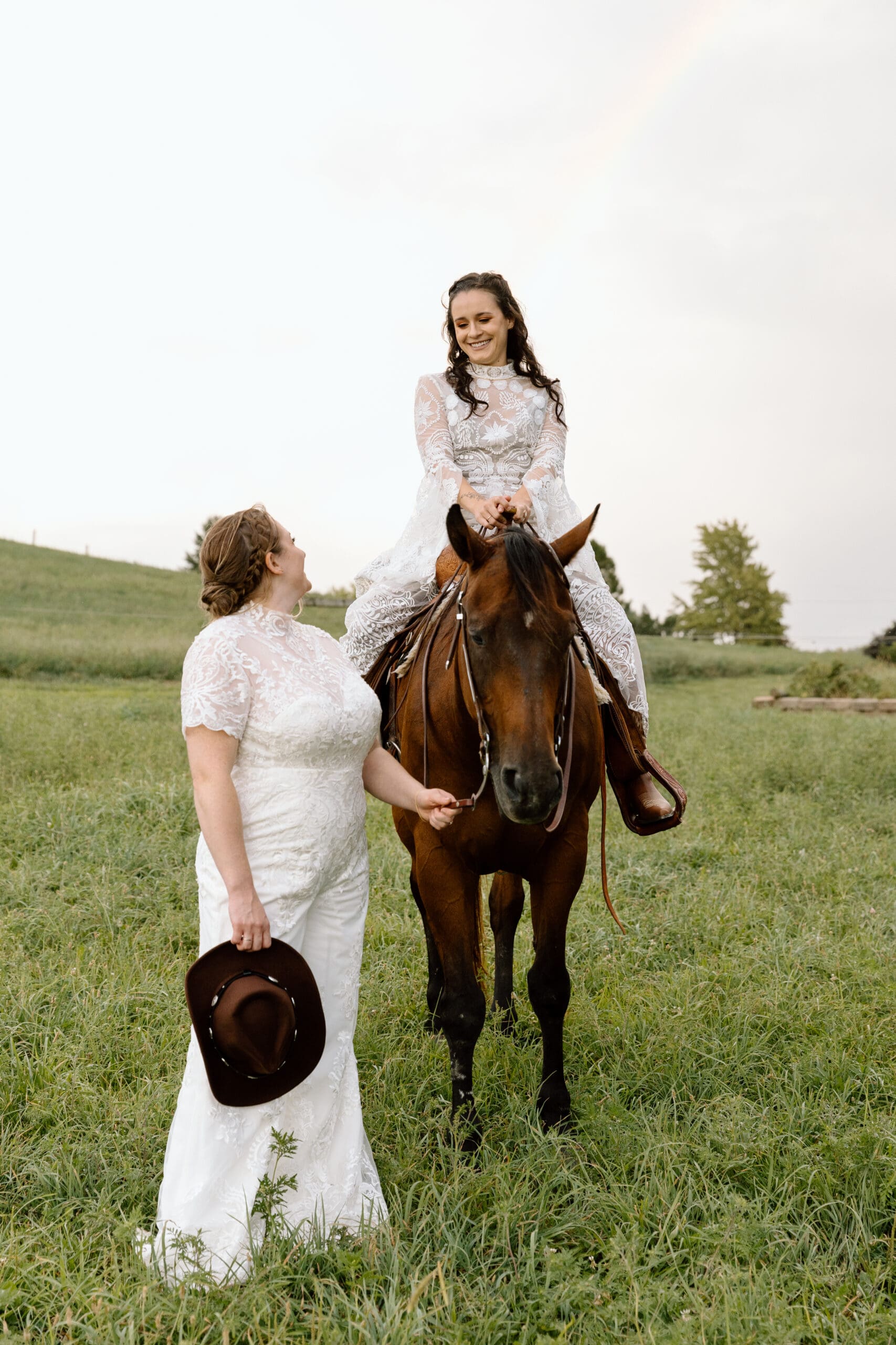 Two brides, one riding a horse, one standing in front of the horse.