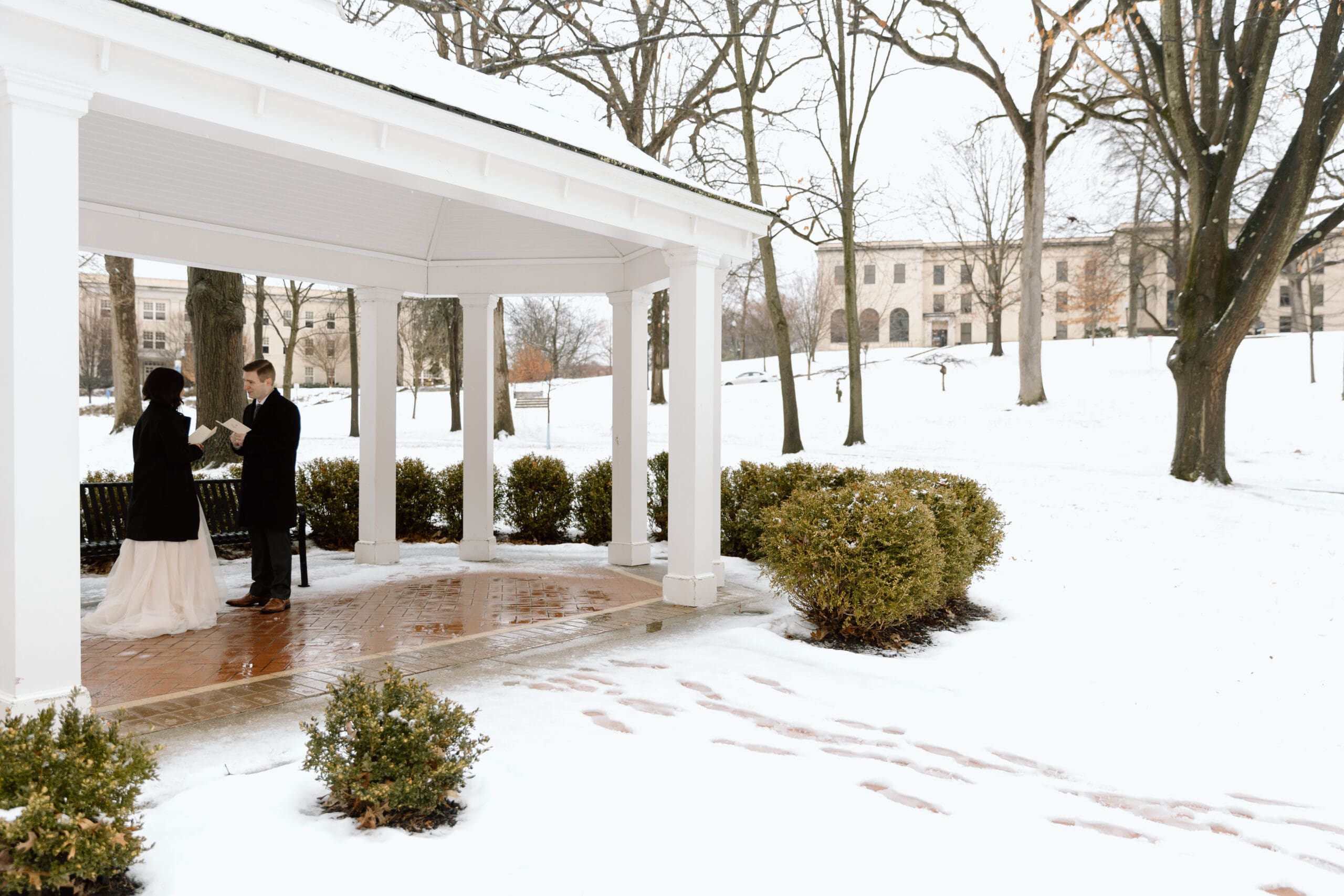 Couple saying their vows under a gazebo on a snowy day.