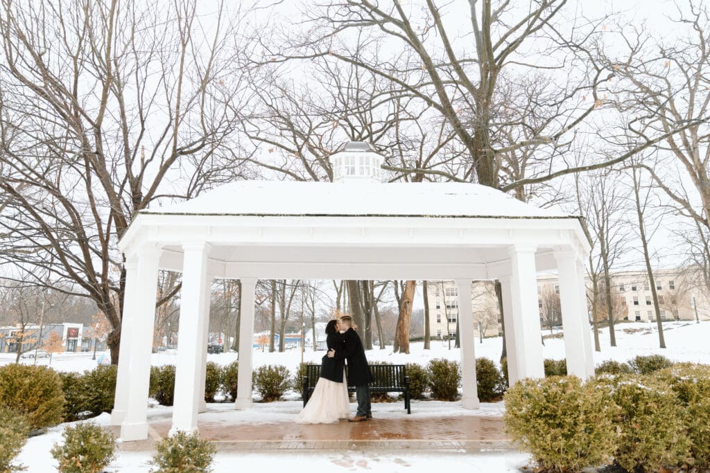Couple kissing under a gazebo on a rainy and snowy day.