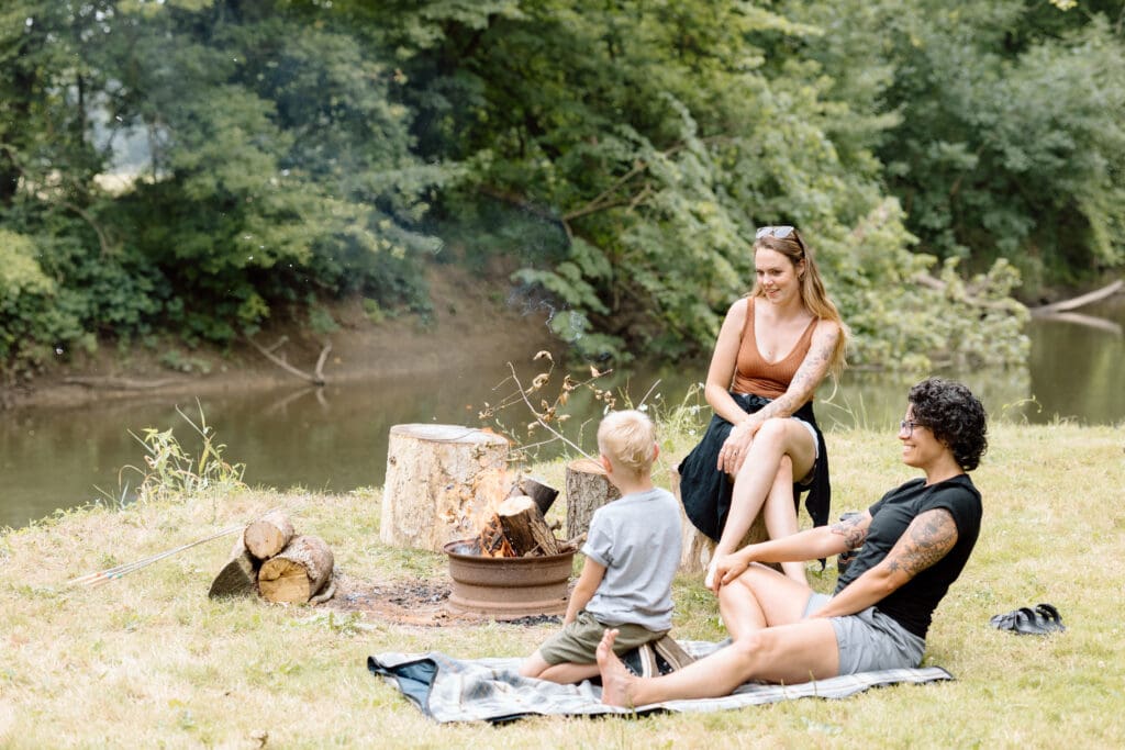 Family sitting around a campfire next to a river.