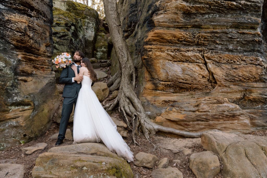 Eloping couple embracing in front of a tree and rock formations at Ledges in Cuyahoga Valley National Park.