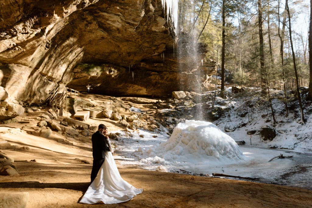 Couple embracing at Ash Cave with the waterfall in the background at Hocking Hills State Park in Ohio.