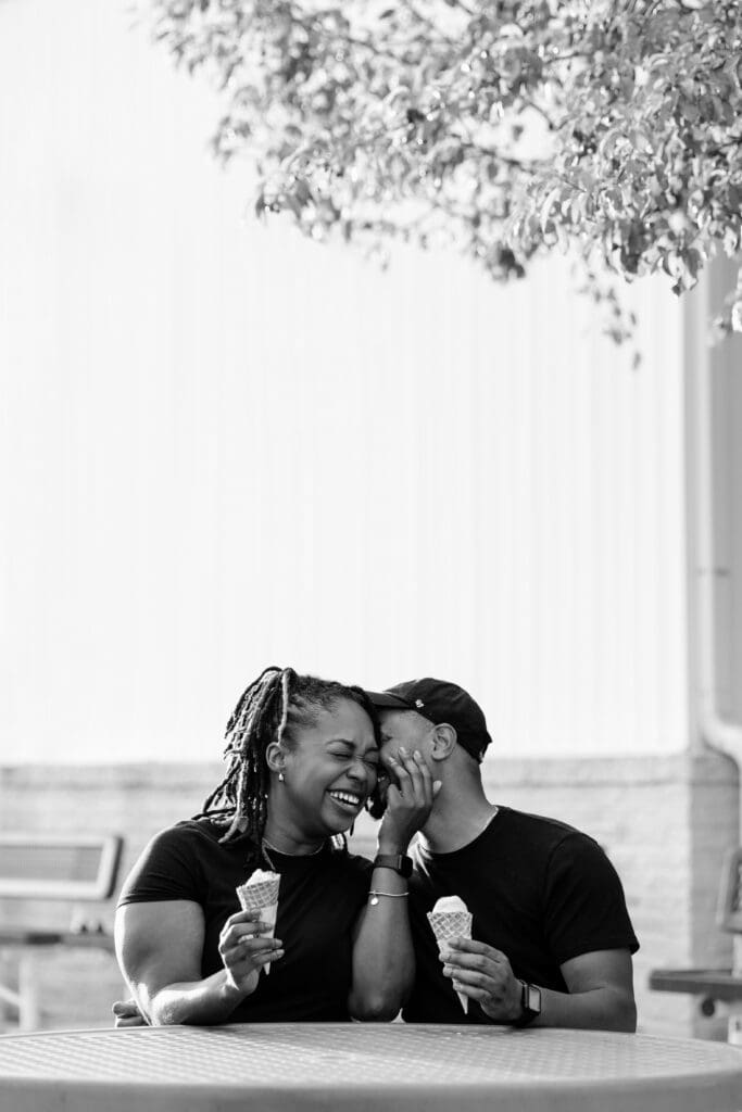 Man whispering in girlfriend's ear while they hold ice cream cones.