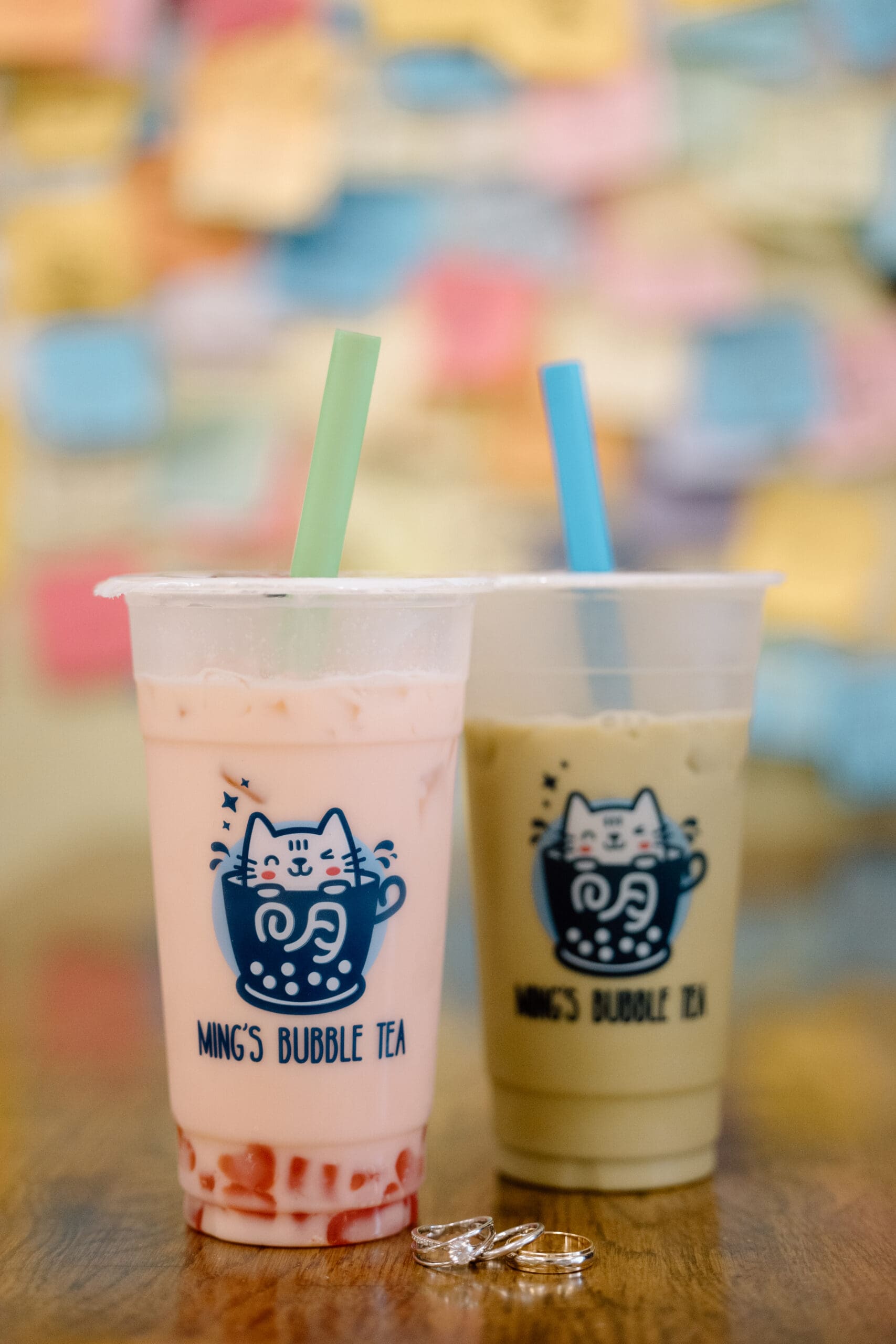 A pink and green bubble tea with wedding rings in front of them.