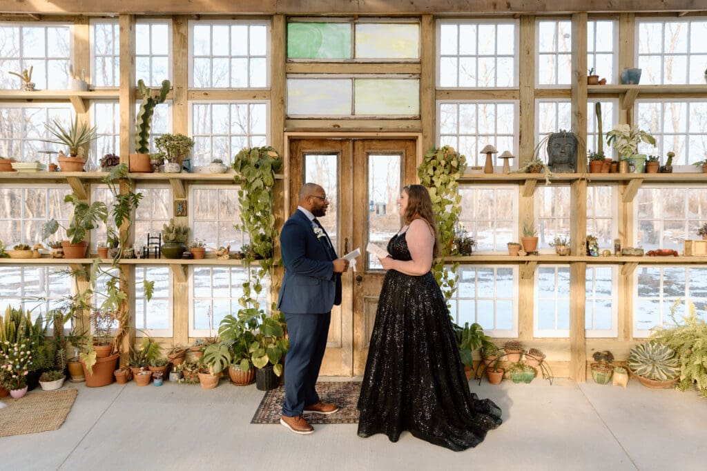 Couple reading vows in a greenhouse with snow outside.