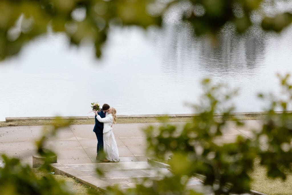Couple kissing at Wade Lagoon while framed by greenery.