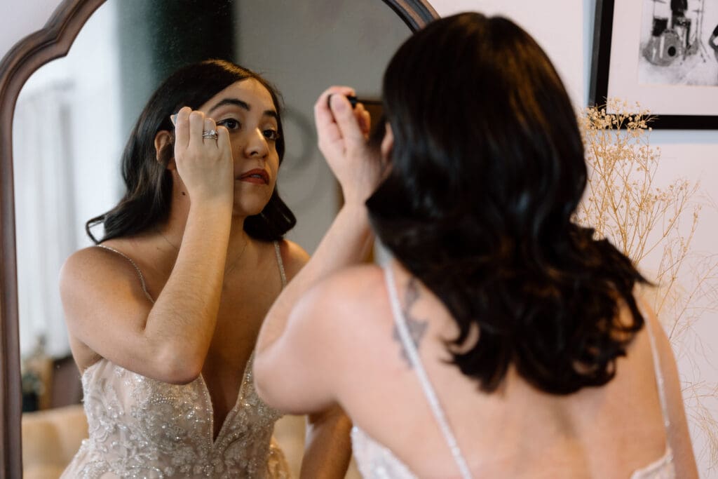Bride putting on eyeliner in a mirror.