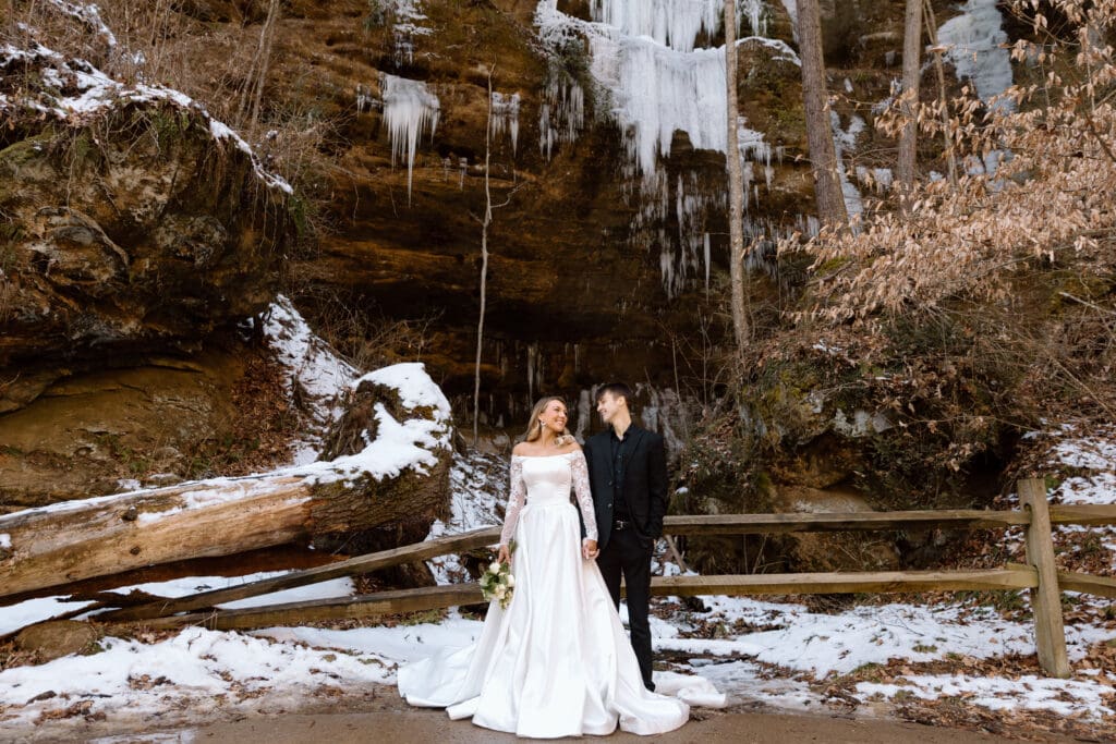 Couple holding hands and looking at each other with snowy icicles behind them in Hocking Hills.