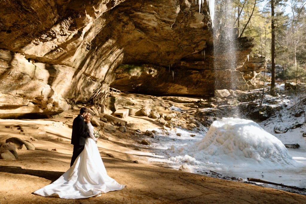 Elopement couple standing next to the frozen Ash Cave waterfall in winter.