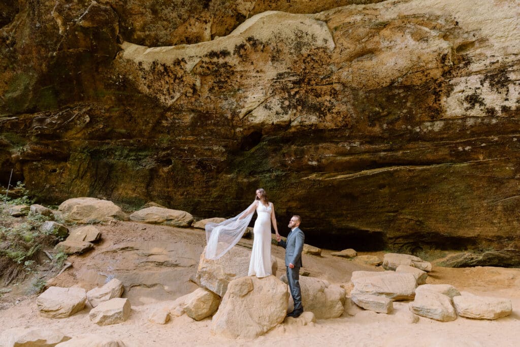 Bride standing on a rock while her groom holds her hand at Ash Cave.