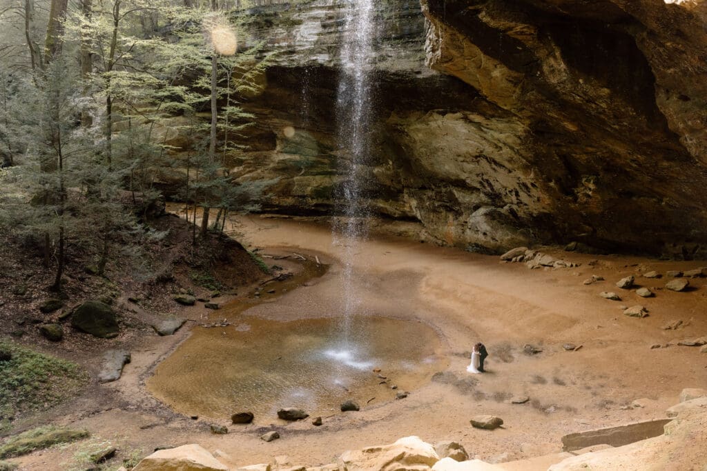 Couple near waterfall at Ash Cave in a wide shot of the cave.
