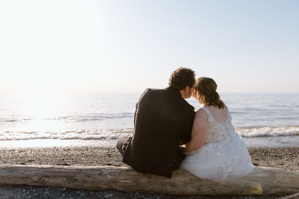 Eloping couple sitting on a log on the beach. 