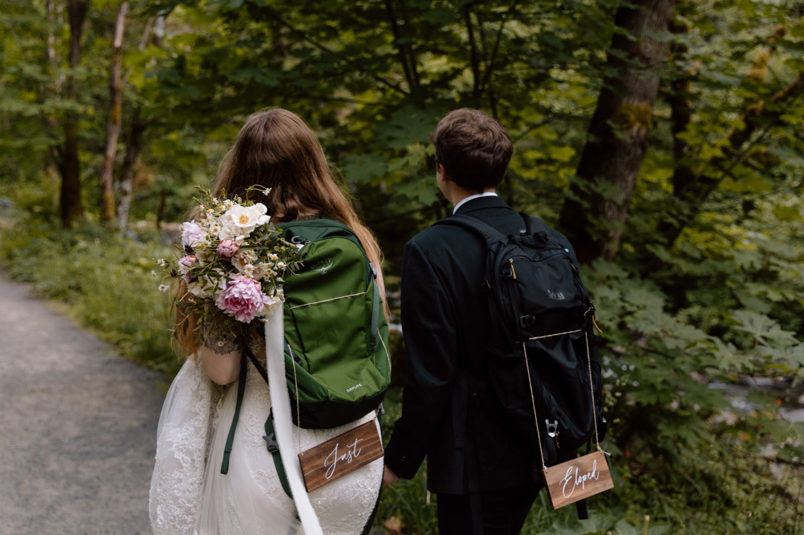 Elopement couple with backpacks walking down a trail in Oregon's Columbia River Gorge.