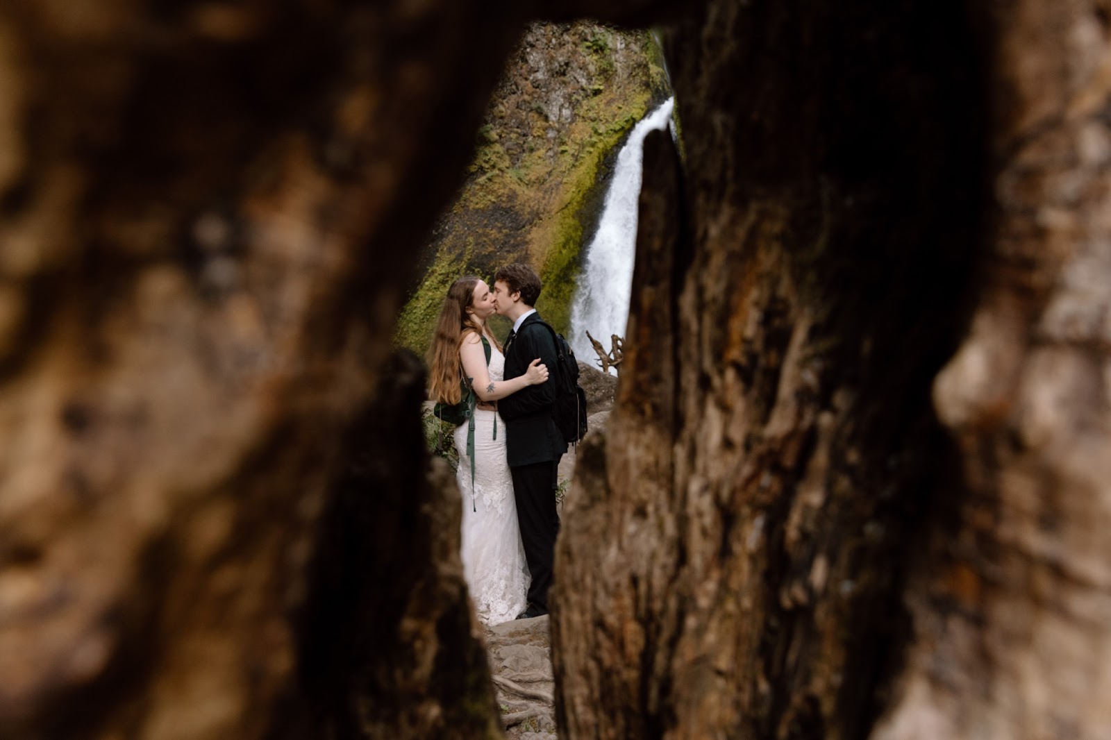Couple eloping in front of a waterfall shown in the middle of a crack in a tree in the Columbia River Gorge.