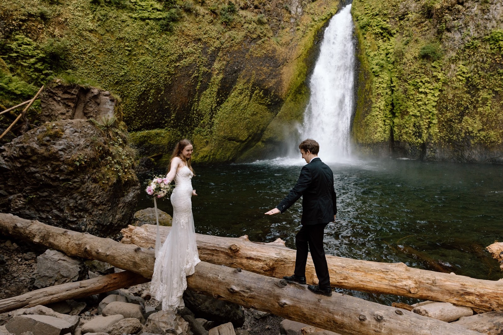 Couple balancing on a fallen log in front of a waterfall in Oregon.