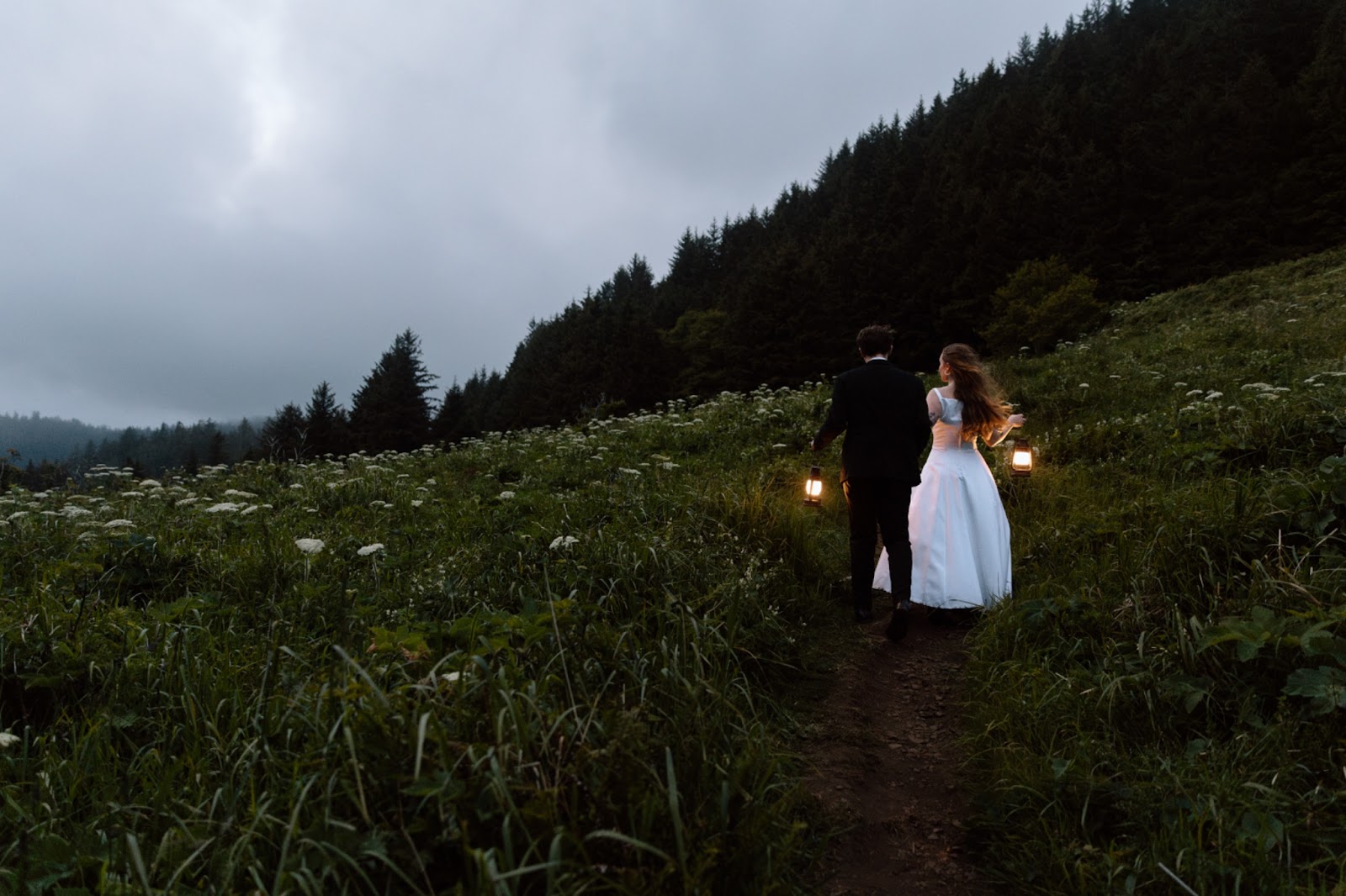 Couple holding lanterns and walking at night through a field on the Oregon Coast.