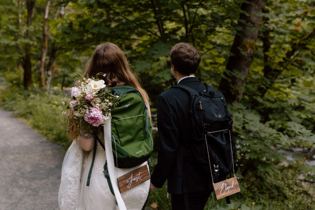 Couple walking with backpacks with signs that say just eloped.