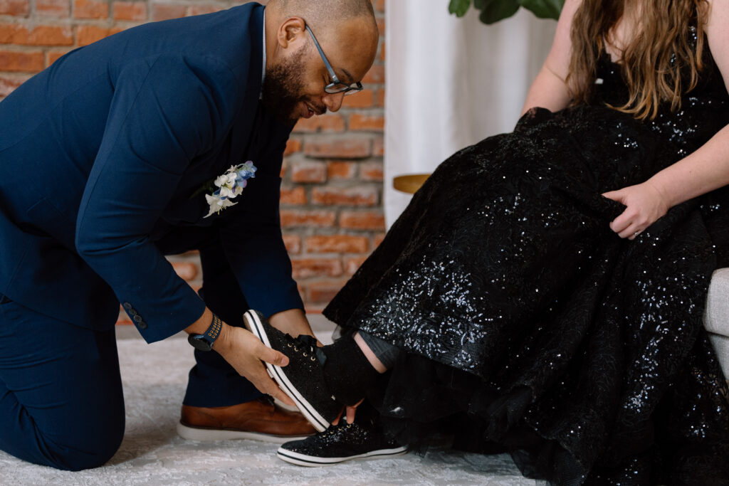 Groom helping bride with her shoes.