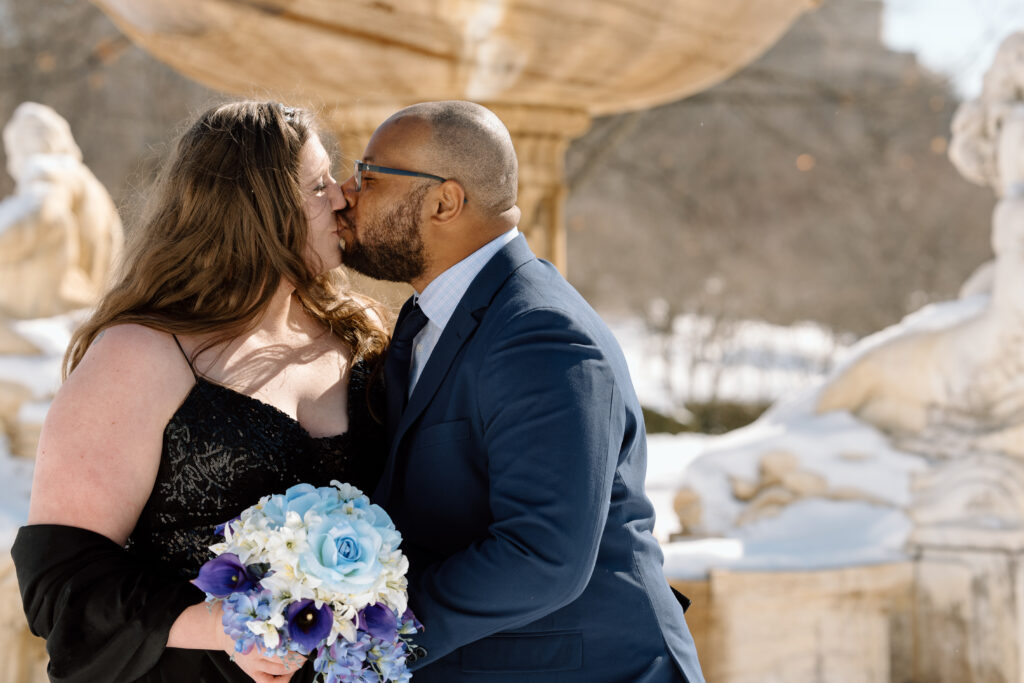 Bride and groom kissing in front of a fountain in front of the Cleveland Museum of Art.