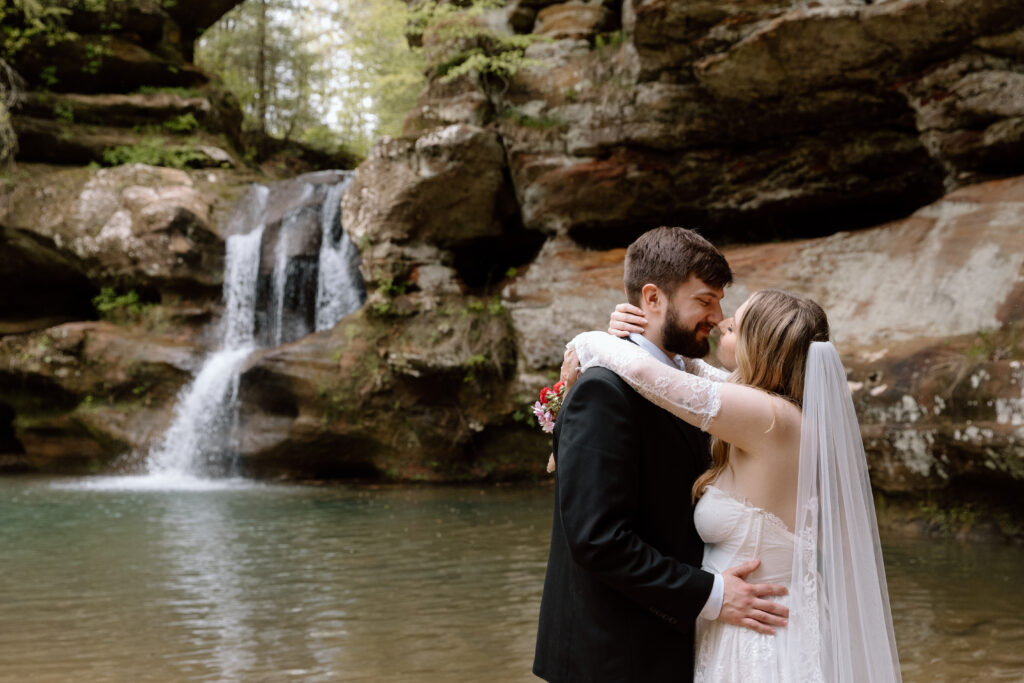 Couple leaning in for a kiss at Upper Falls in Old Man's Cave in Hocking Hills during a spring elopement.