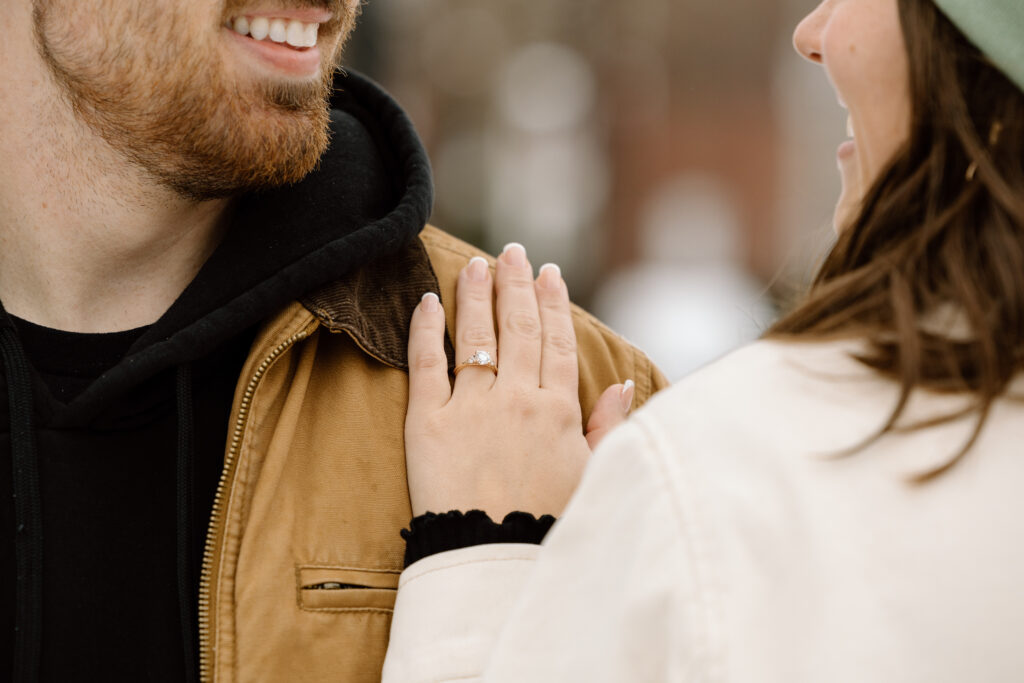 Close up of woman's hand on man's shoulder with the engagement ring.
