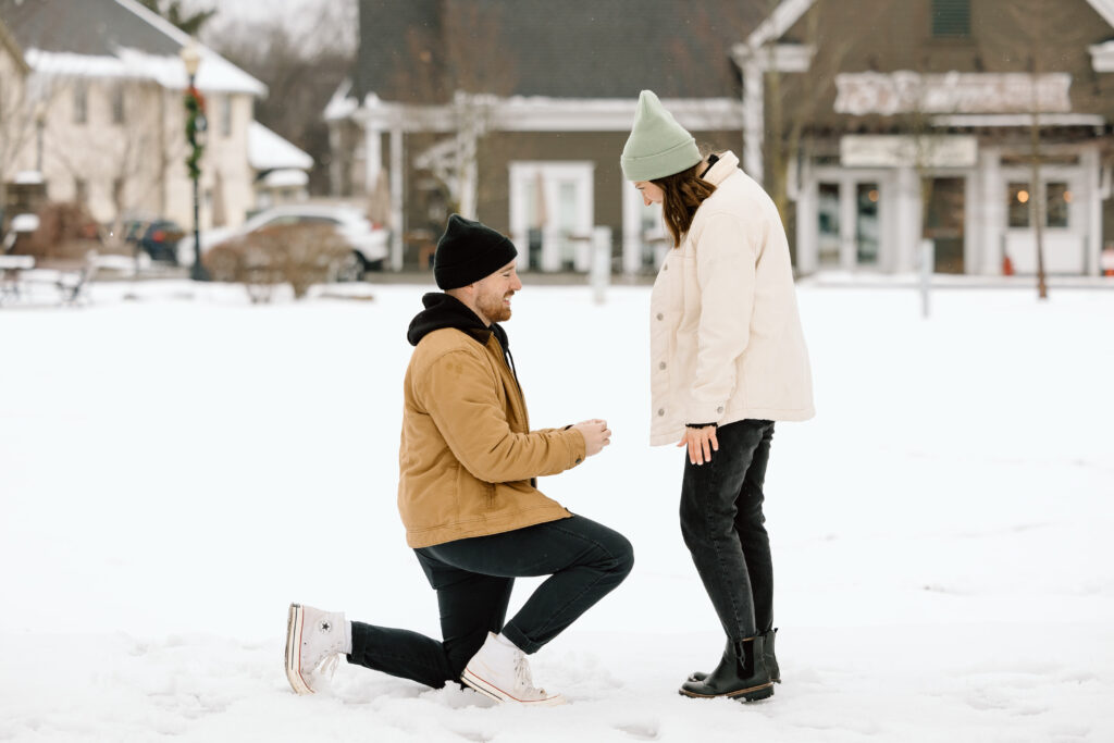 Man down on one knee proposing to his girlfriend in downtown Hudson, Ohio. There is snow all around them.