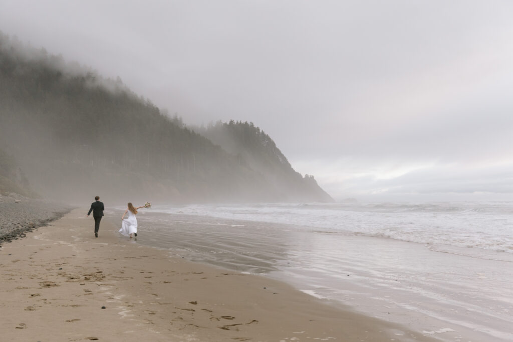 Elopement couple running down a foggy beach on the Oregon Coast.
