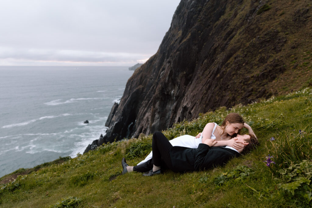 Couple laying down near a cliff looking out on the Pacific Ocean.