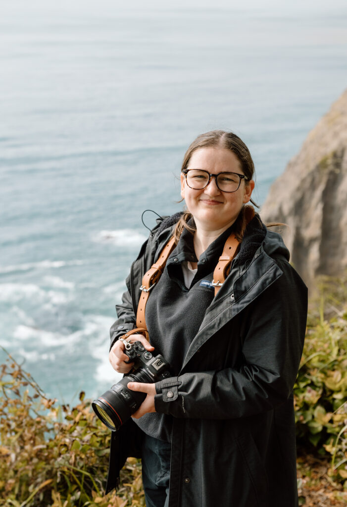 Desiree holding her camera with the ocean behind her.