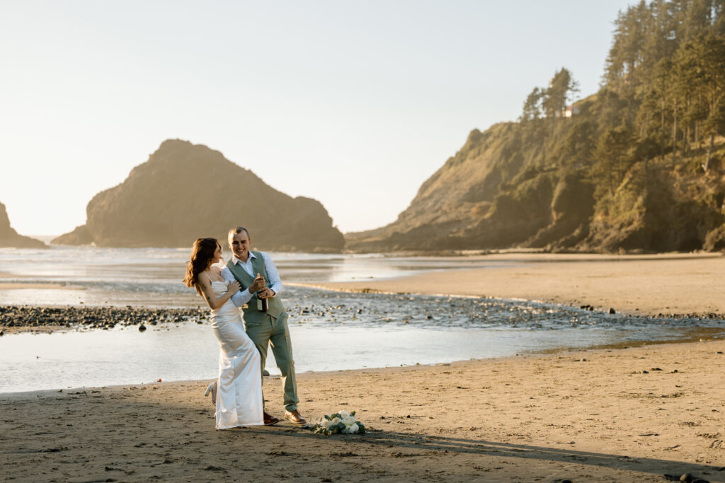 Bride embracing groom as he gets ready to pop the sparkling tea on Heceta Head Beach.