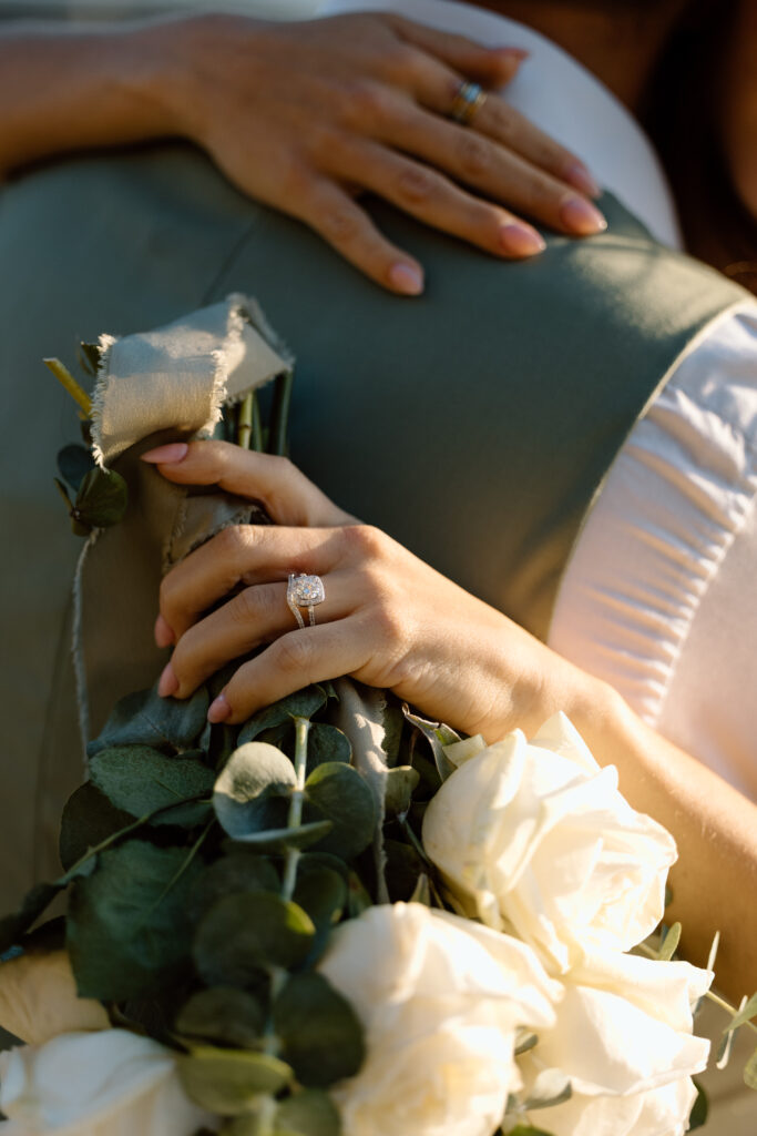Close up of ring and flowers while bride hugs groom.