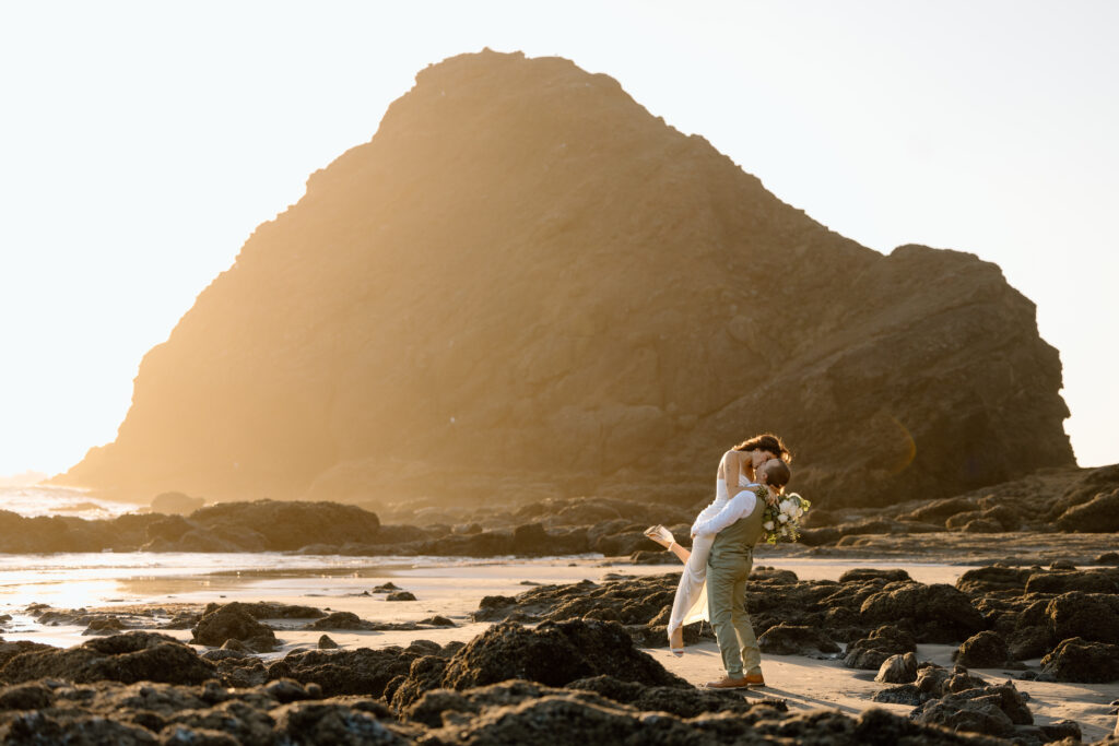 Groom lifting up bride with a sea stack behind them on Heceta Head Beach.