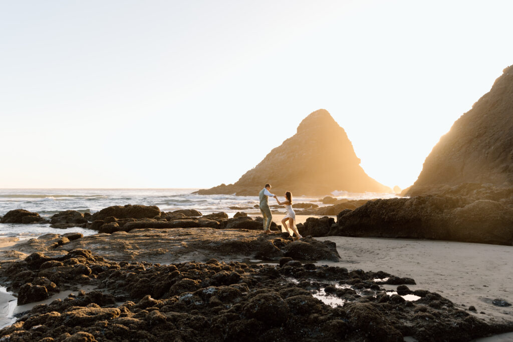 Groom helping bride up on the rocks at the beach.