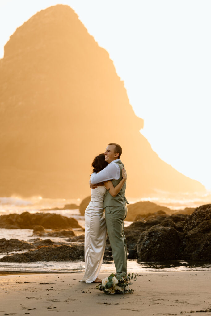 Couple hugging with the sunset light hitting the sea stack behind them.
