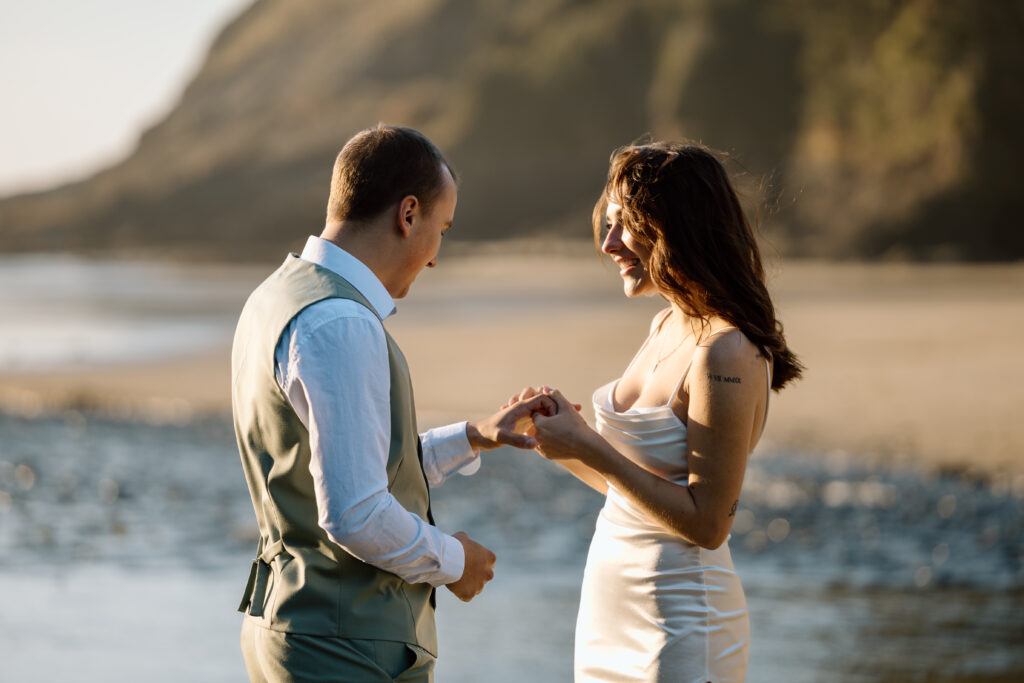 Bride putting wedding band on groom's hand.
