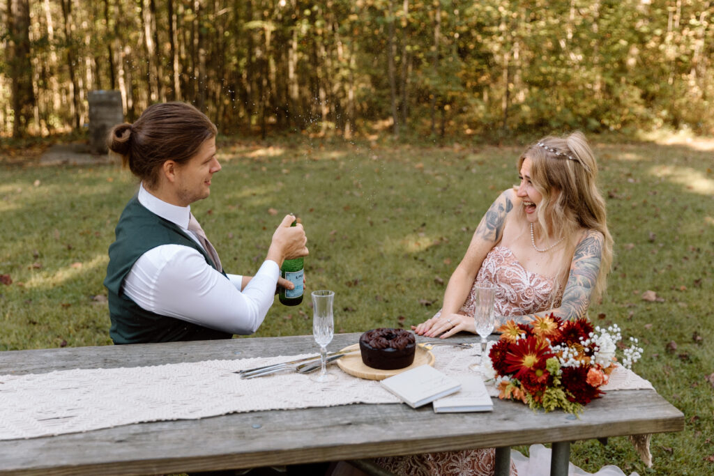 Groom shaking and spraying sparkling water at a picnic bench. 