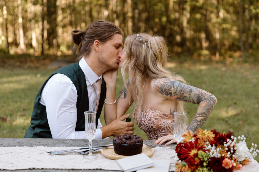 Couple kissing over their cake on a picnic benhc.