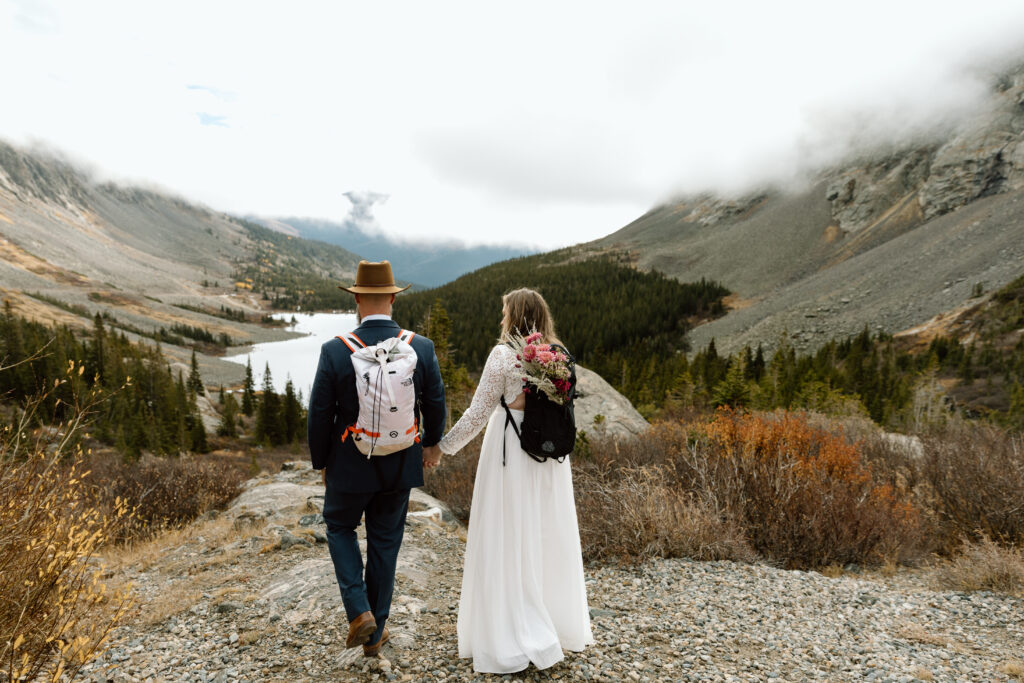 Couple hiking to a rocky outcrop in front of a lake and mountains.