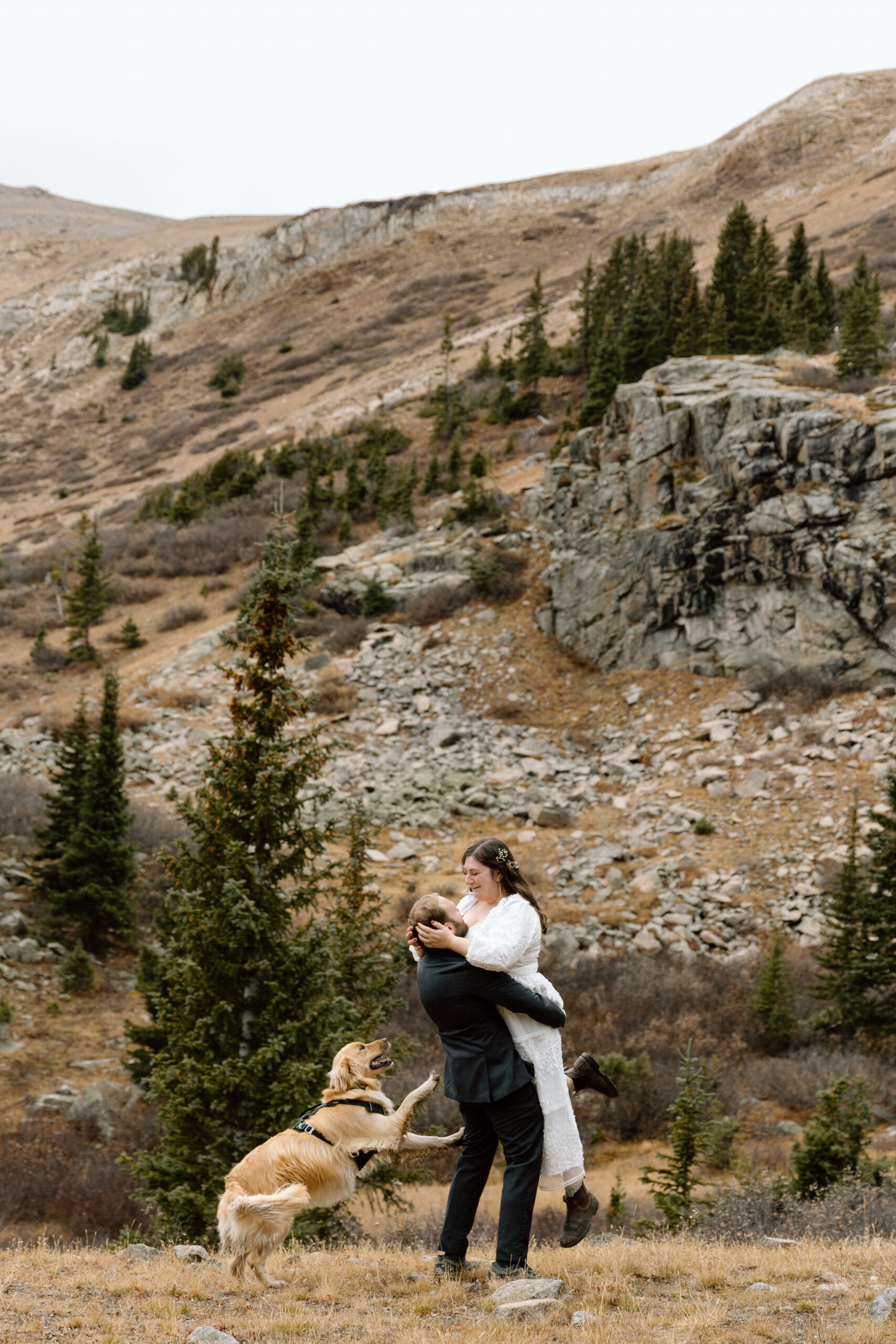 Couple spinning around and their dog prancing behind them in the Colorado mountains.