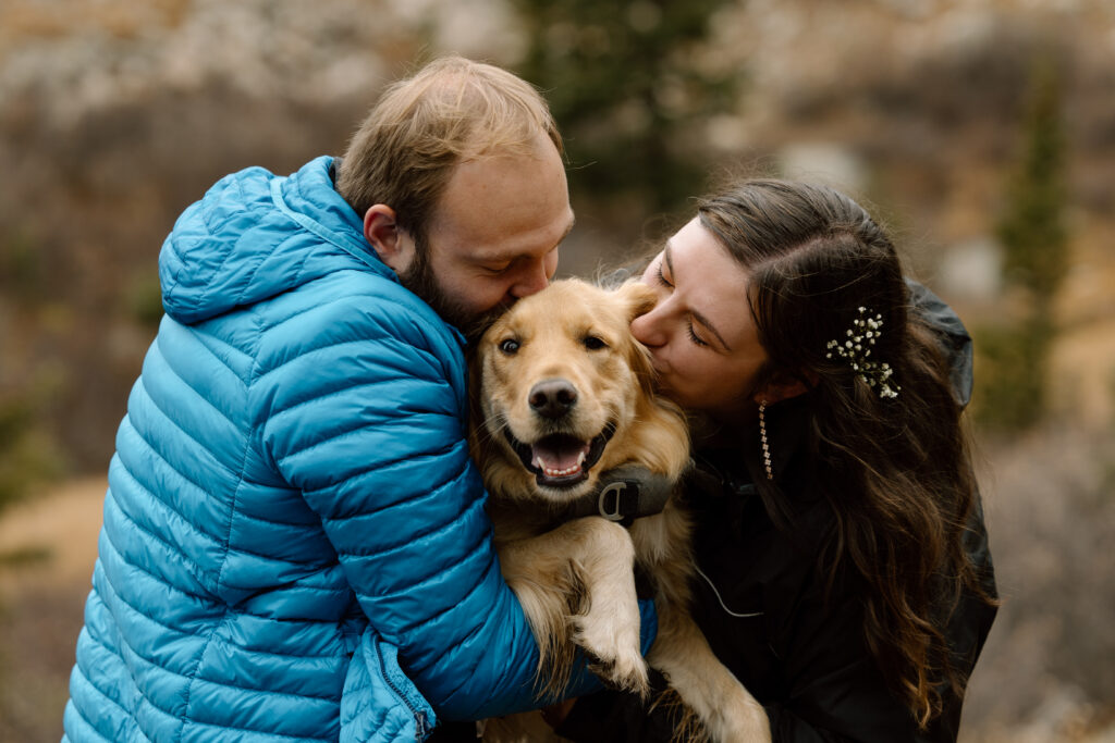 Couple holding up and kissing their dog on its head during their elopement.