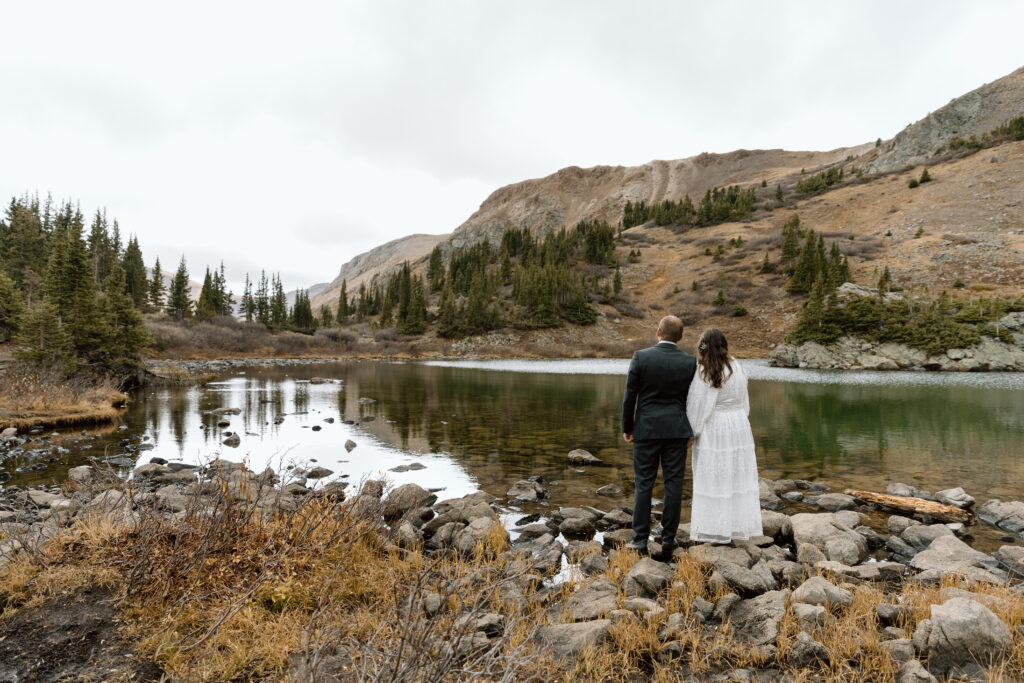 Couple holding hands and looking out on an alpine lake.
