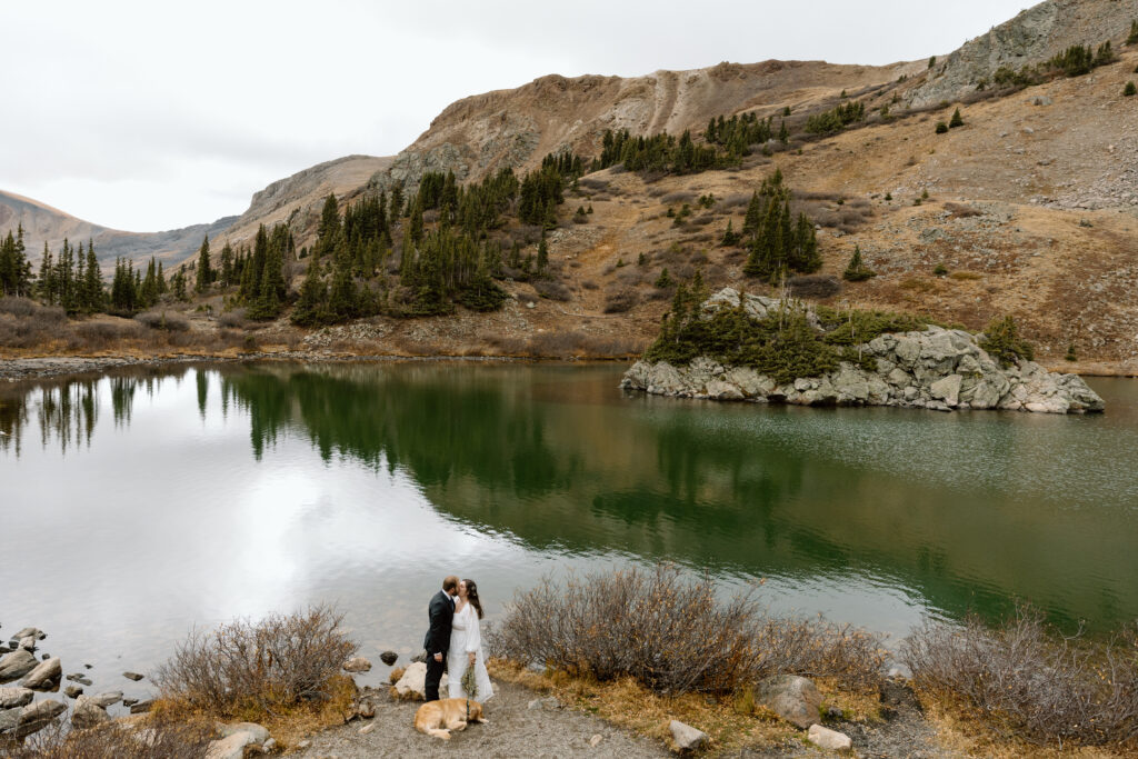 Couple kissing in front of an alpine lake.