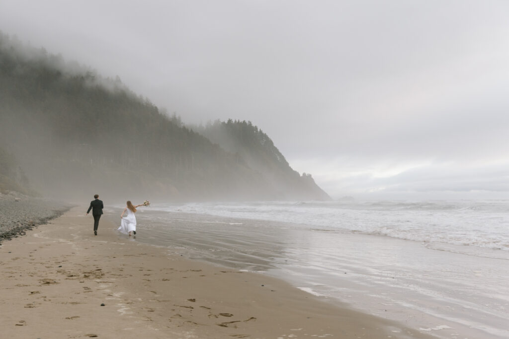 Eloping couple running on a deserted beach on the Oregon Coast.