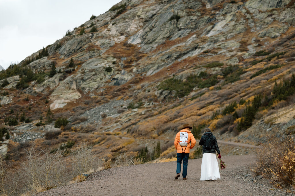 Couple in backpacks and puffy jackets hiking up a trail in the Colorado mountains.