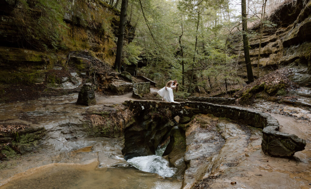 Elopement couple doing a dip kiss on a stone bridge above Devil's Bathtub in Hocking Hills.