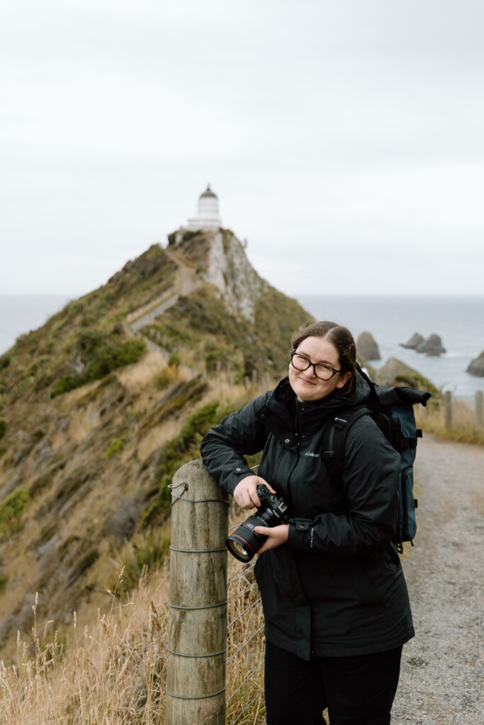 Desiree holding her camera with a lighthouse behind her.