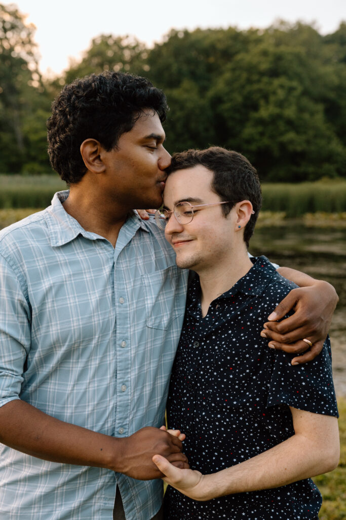 Couple holding hands and kissing the other on the forehead.