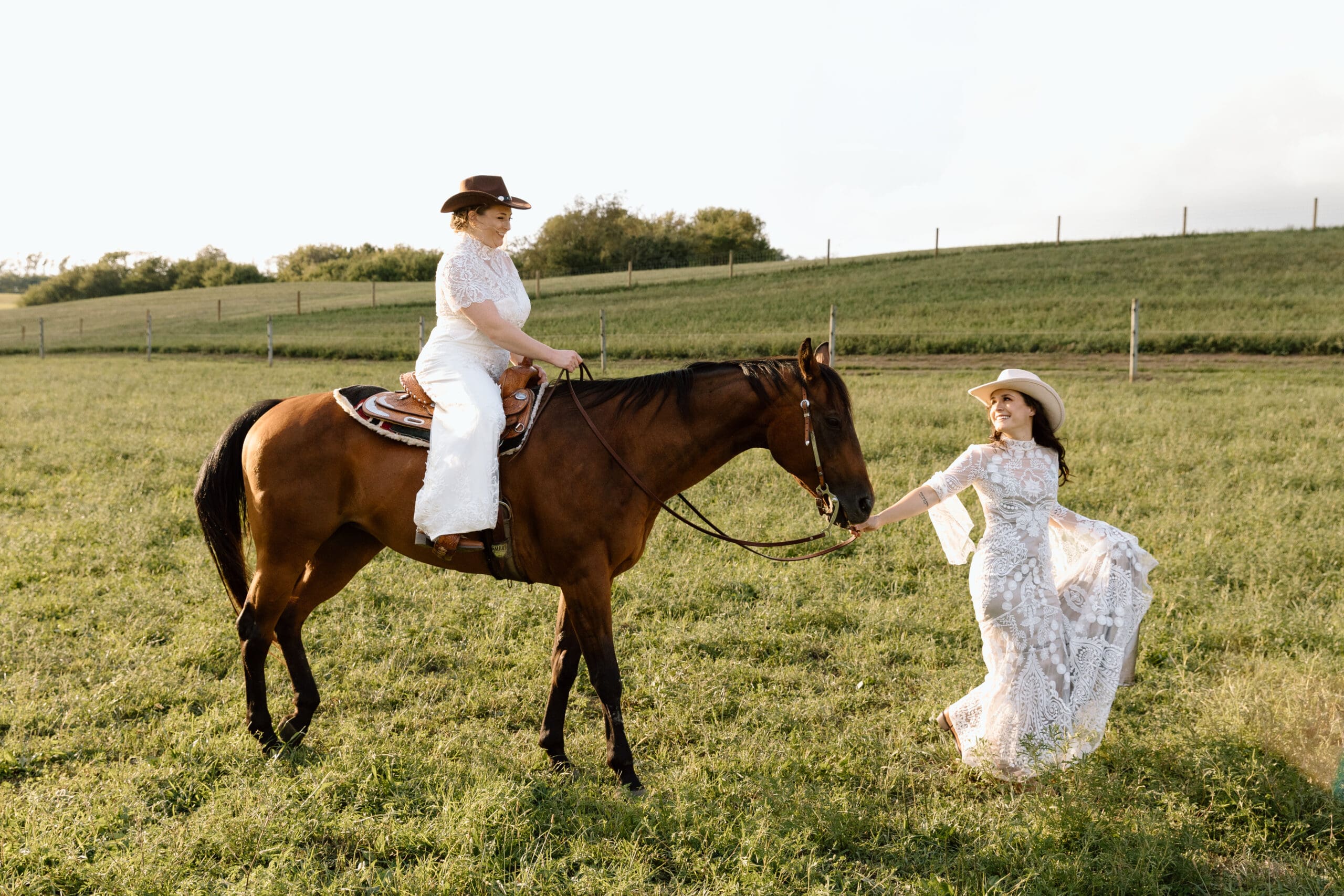 Two brides, one is leading a horse, her partner is sitting on the horse.