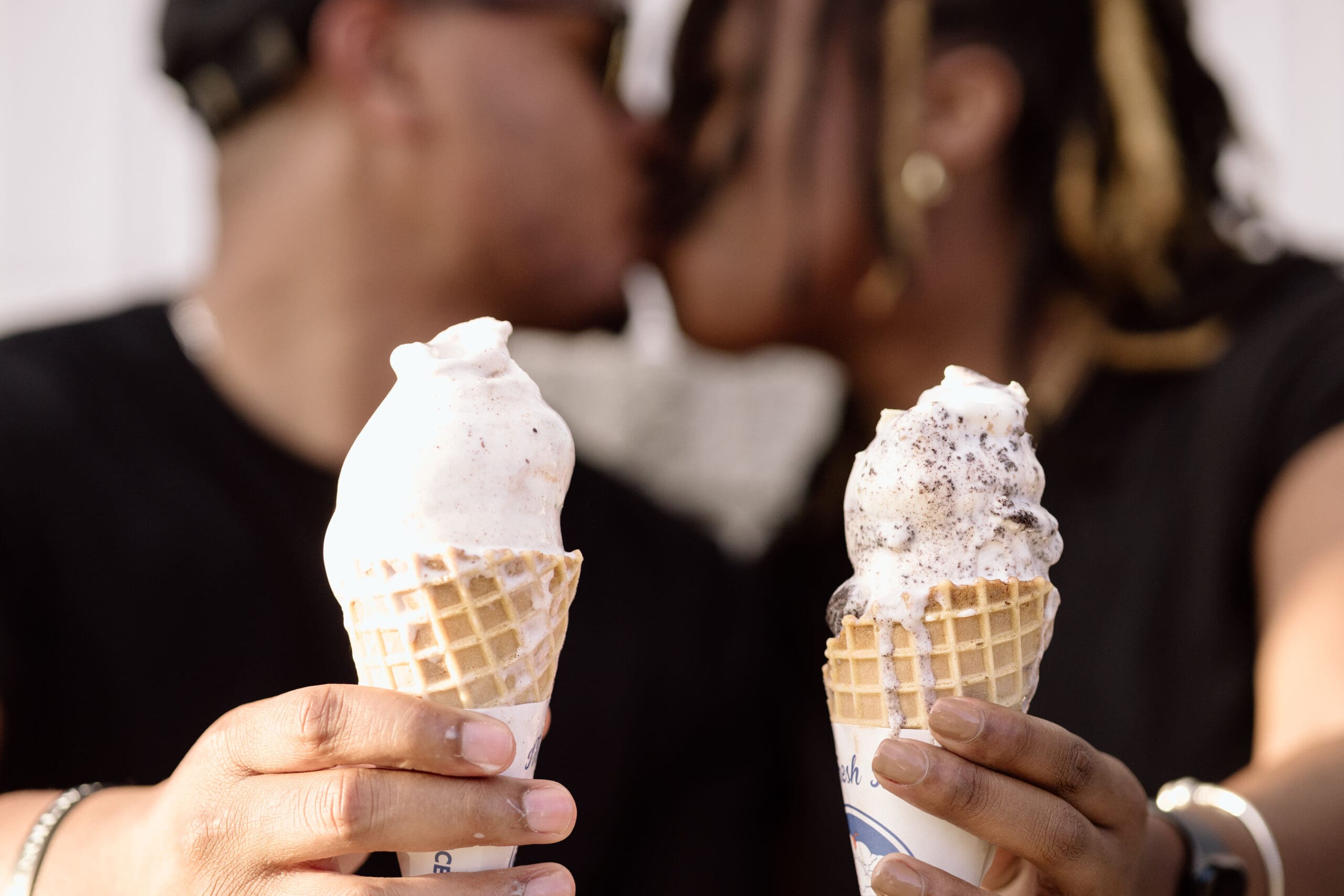 Couple holding out their ice cream cones while kissing.