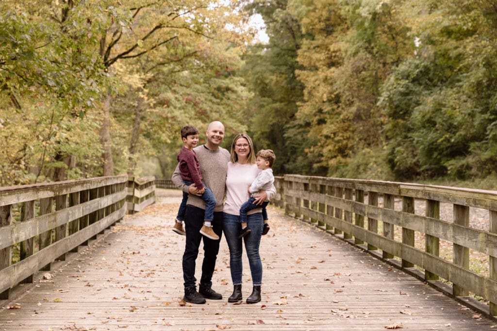 Family of four standing in the middle of a wooden bridge at Sand Run Metro Park in Akron, OH.